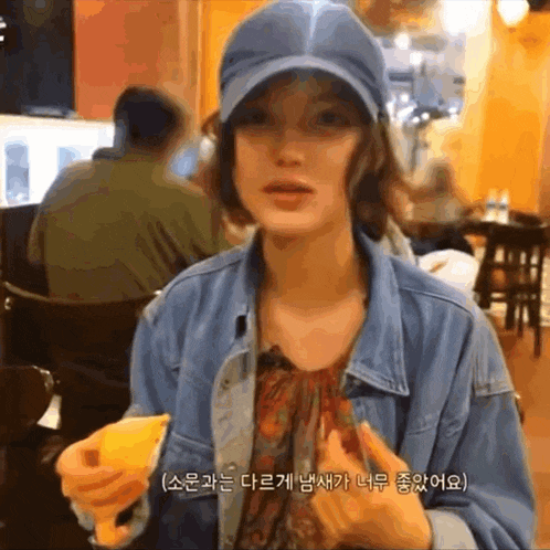 a woman wearing a blue hat and a denim jacket is holding a slice of pizza