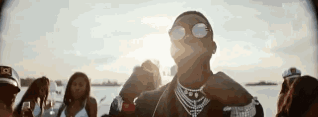 a man wearing sunglasses and a necklace is standing in front of a crowd of people .