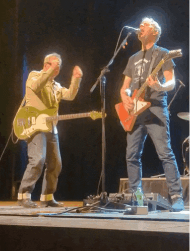 a man singing into a microphone while another man plays a guitar on stage