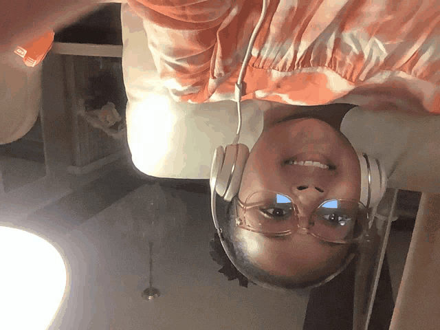 a woman wearing headphones and glasses is upside down and smiling