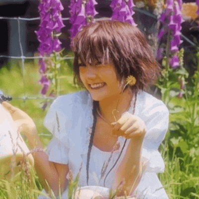 a woman in a white dress is sitting in the grass with purple flowers behind her