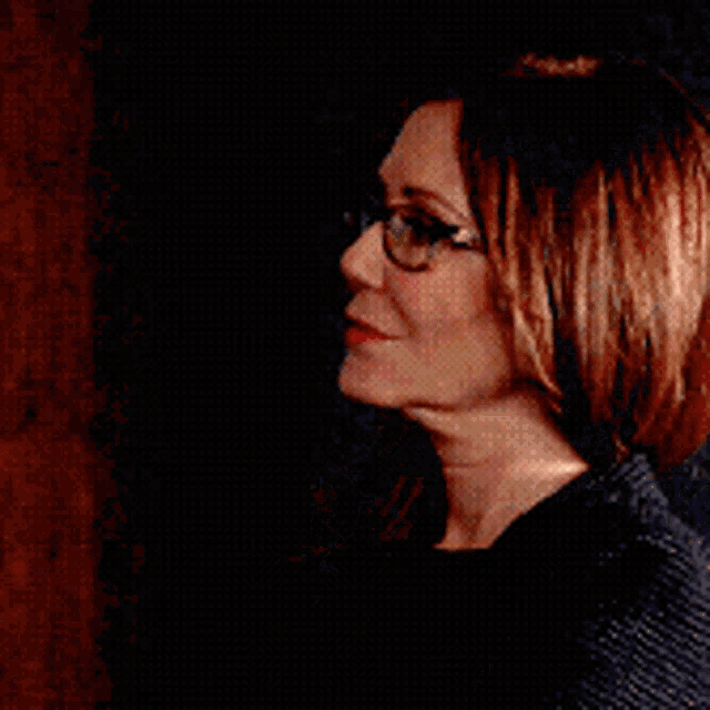 a woman wearing glasses and a black jacket looks serious