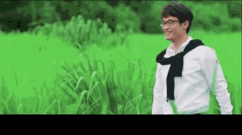 a man wearing glasses and a scarf is standing in a field of green grass .