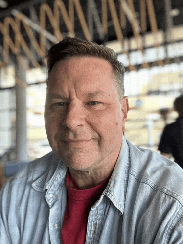 a man wearing a red shirt and a denim shirt is smiling