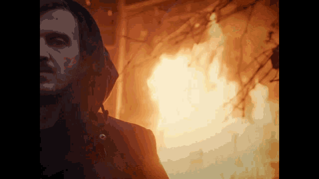 a man in a hooded jacket stands in front of a burning building