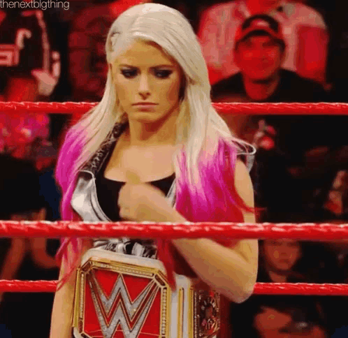 a woman with pink hair is standing in a wrestling ring holding a wrestling championship belt .