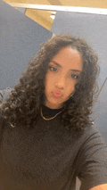 a young woman with curly hair is taking a selfie in a bathroom stall .