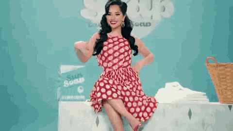 a woman in a red and white polka dot dress is sitting on a laundromat .