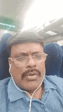 a man wearing glasses and ear buds is sitting in a blue seat
