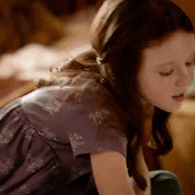 a young girl wearing a purple dress is looking down