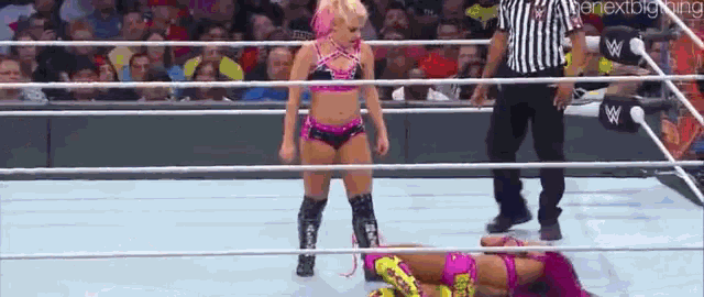 a woman is standing in the middle of a wrestling ring while another woman is laying on the ground .