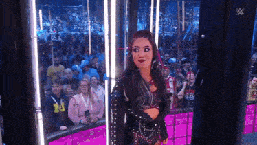 a female wrestler is standing in front of a crowd in a cage .