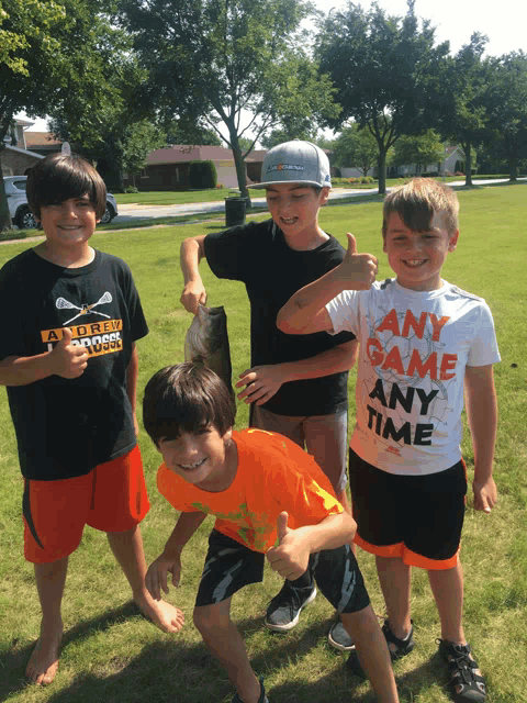 a boy wearing a shirt that says " any game any time " holds a fish