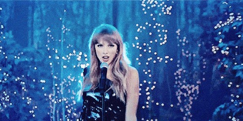 a woman in a black dress is singing into a microphone in a dark forest .