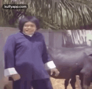 a man in a blue jacket is standing in front of a fence with a goat .