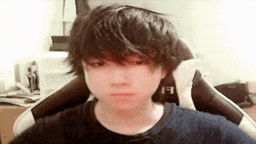 a young boy with long hair is sitting in a chair making a funny face .