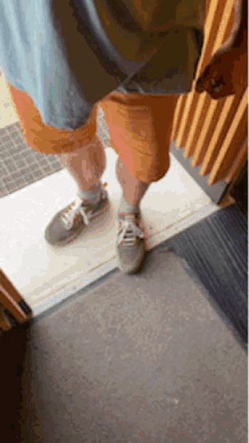 a person wearing orange shorts and green shoes standing on a doorstep