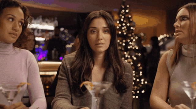 three women are sitting at a table with martini glasses