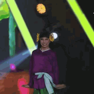 a woman wearing a purple shirt and green skirt is dancing