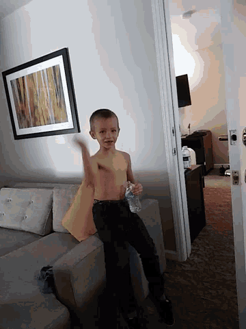 a shirtless boy holds a bottle of water in a living room