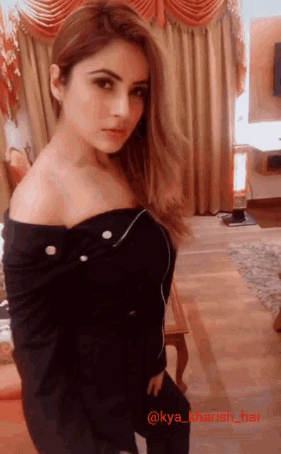 a woman in a black off the shoulder top is standing in front of a window