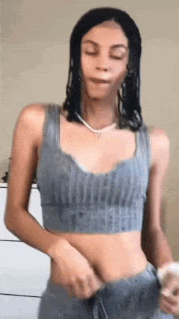 a woman wearing a crop top and sweatpants is standing in front of a white dresser .