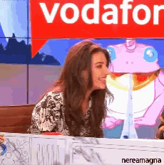 a woman sits at a desk in front of a sign that says vodafone