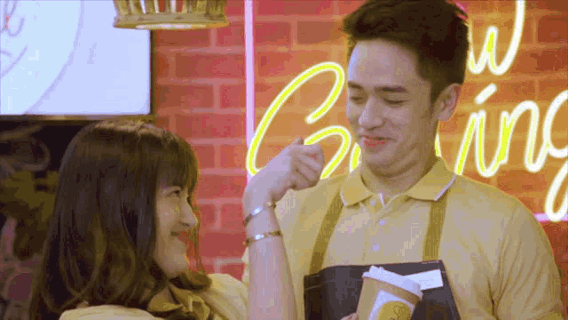 a man and a woman are looking at each other in front of a neon sign that says " giving "
