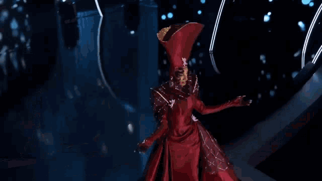 a woman in a red dress is walking down a runway while a woman in a pink dress stands behind her .