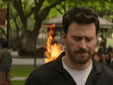a man in a black jacket is standing in front of a fire .