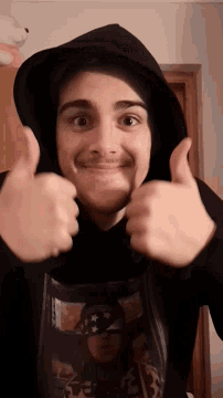 a young man wearing a black hoodie giving a thumbs up