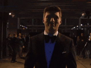 a man in a tuxedo is walking through a dark hallway with a red exit sign above him
