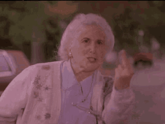 an elderly woman is giving the middle finger while wearing a pink sweater .