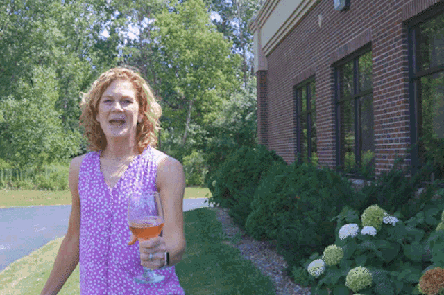 a woman in a pink tank top holds a glass of wine in front of a brick building