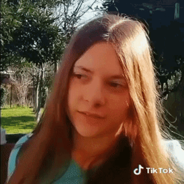 a young girl with long hair is standing in a park .