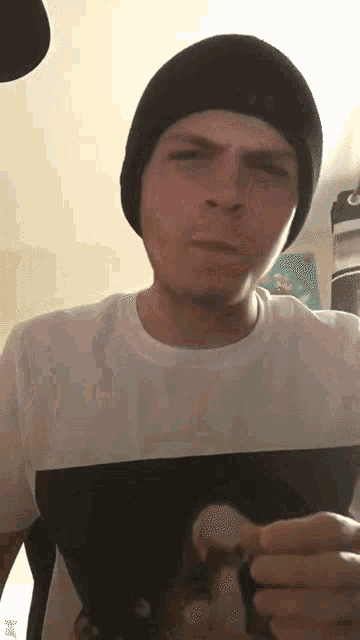 a man wearing a black beanie and a white t-shirt is holding something in his hand .