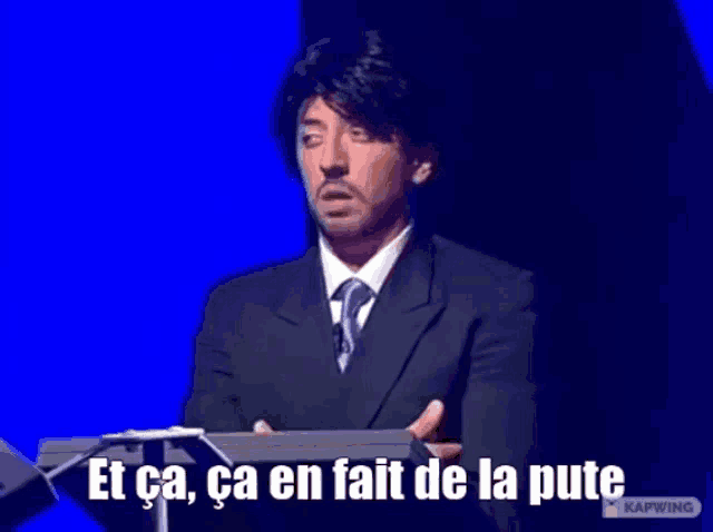a man in a suit and tie stands at a podium with the words et ca ca en fait de la pute