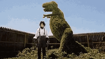 a man standing next to a t-rex made of plants