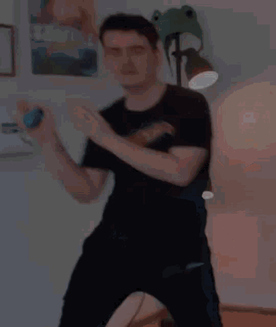 a man in a black shirt is dancing in a room with a lamp and a frog hat .