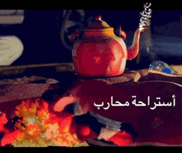 a red teapot sits on a table next to a fire with arabic writing below it