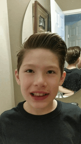 a young boy smiles in front of a mirror with a framed picture on the wall behind him