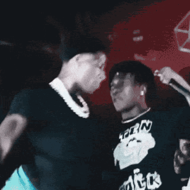 two men are dancing in a dark room and one of them is wearing a shirt that says ' tpe ' on it .