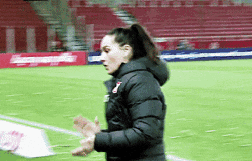 a woman in a black jacket is walking on a soccer field ..