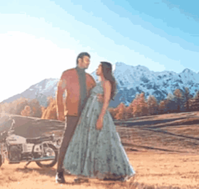 a man and a woman are standing next to each other in a field with mountains in the background .