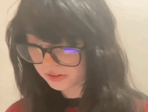 a young girl wearing glasses and a red shirt is looking at the camera .