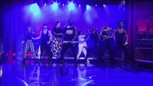 a group of people are dancing on a stage with a man wearing a shirt that says dope