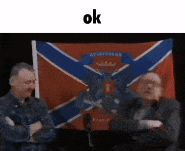 two men are shaking hands in front of a flag that says ' ok ' on it .