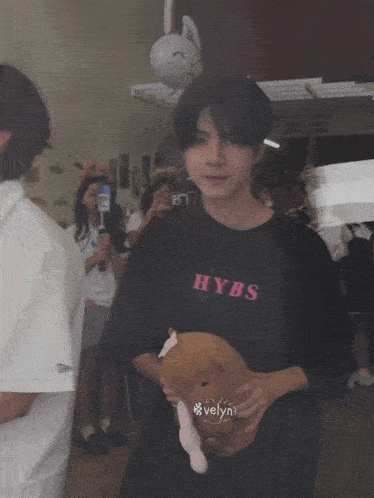 a boy wearing a hybs t-shirt holds a stuffed animal