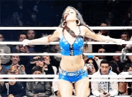 a woman in a blue top and shorts is standing in a ring with her arms outstretched