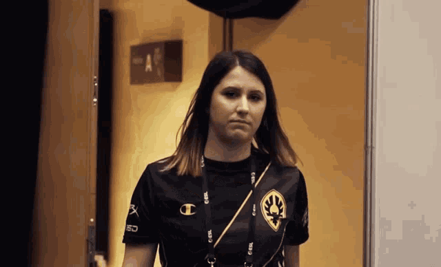 a woman wearing a black shirt with a gold logo on it